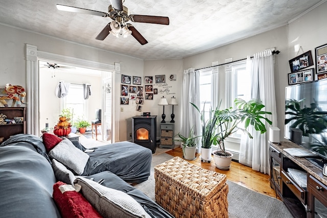 living room featuring a wood stove, ceiling fan, wood-type flooring, and a textured ceiling