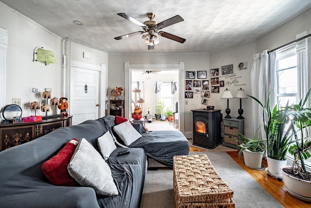 living room with ceiling fan, wood-type flooring, a wood stove, and a textured ceiling