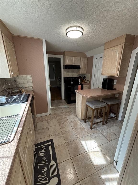 259 Gillette Ave, Springfield, MA 01118 - kitchen with light brown cabinetry, backsplash, a peninsula, a textured ceiling, and under cabinet range hood