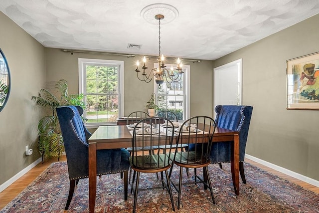 dining area with baseboards, an inviting chandelier, wood finished floors, and visible vents