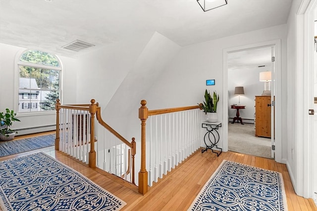 corridor with an upstairs landing, baseboard heating, visible vents, and light wood-style floors