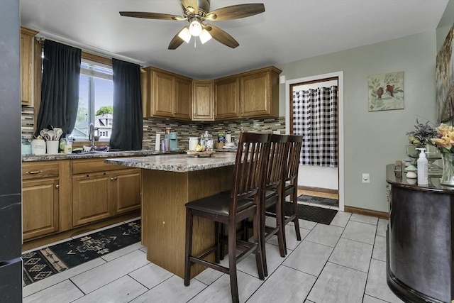 kitchen with a sink, brown cabinets, a breakfast bar, ceiling fan, and decorative backsplash