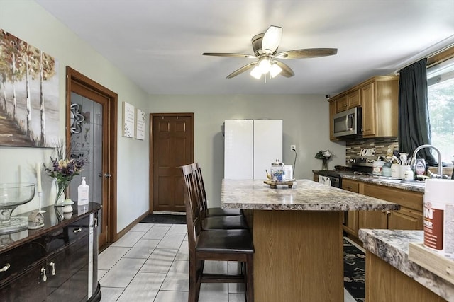 kitchen featuring stainless steel appliances, a kitchen bar, a ceiling fan, decorative backsplash, and a kitchen island