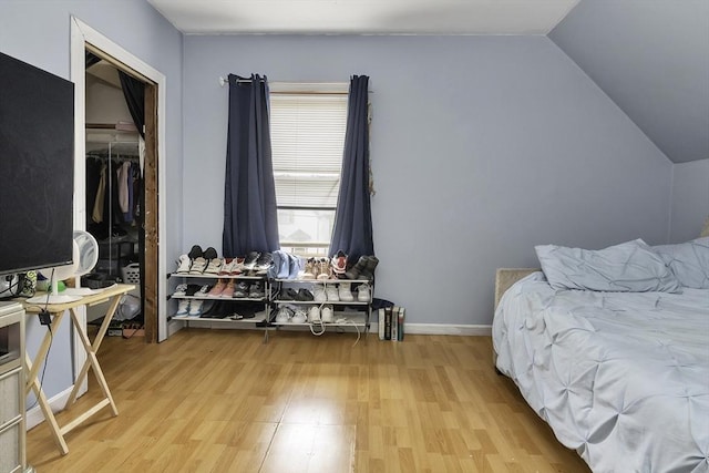 bedroom featuring lofted ceiling, light wood-style flooring, a closet, and baseboards