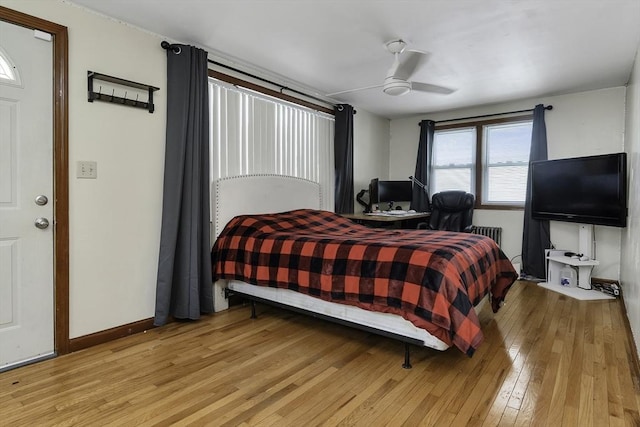 bedroom featuring light wood-style flooring, baseboards, ceiling fan, and radiator heating unit