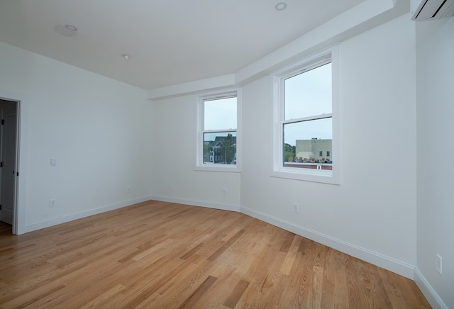 spare room featuring a wall mounted AC and light hardwood / wood-style flooring