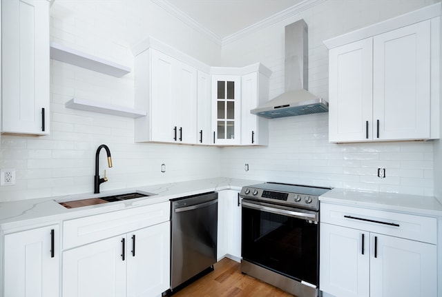 kitchen with white cabinets, light wood-type flooring, appliances with stainless steel finishes, sink, and wall chimney range hood