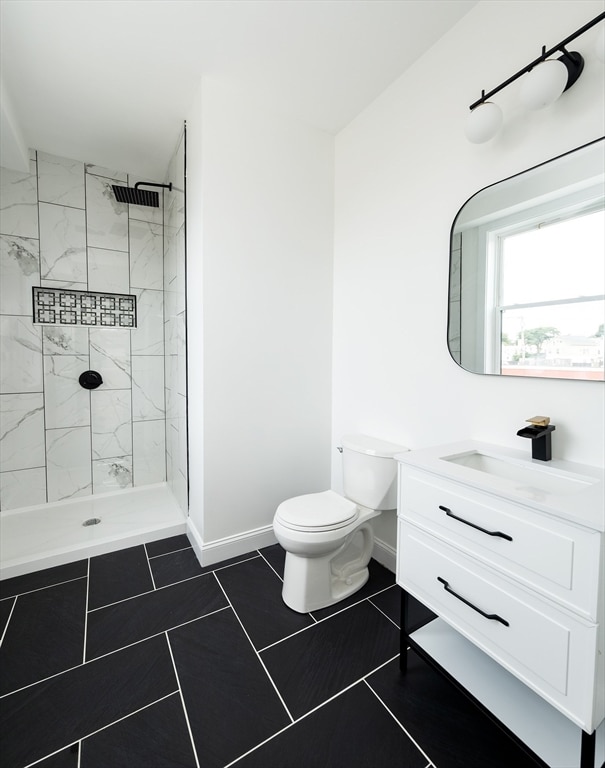 bathroom featuring vanity, toilet, a tile shower, and tile patterned flooring