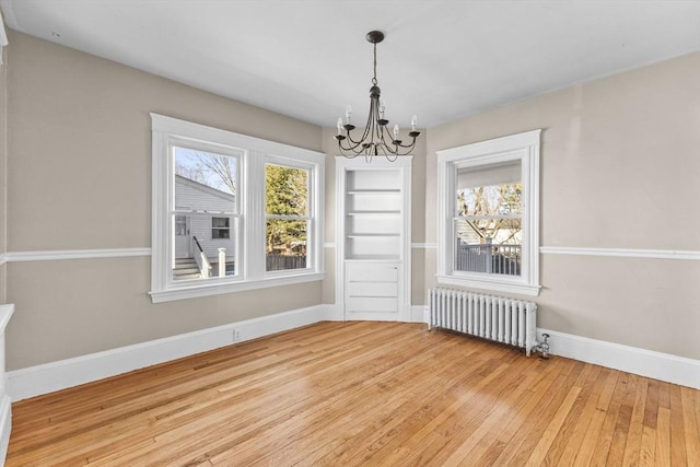 unfurnished dining area with wood-type flooring, plenty of natural light, radiator heating unit, and a chandelier