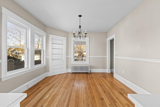 unfurnished dining area with an inviting chandelier, radiator, and light hardwood / wood-style flooring