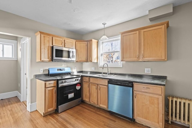 kitchen featuring sink, hanging light fixtures, light hardwood / wood-style flooring, appliances with stainless steel finishes, and radiator