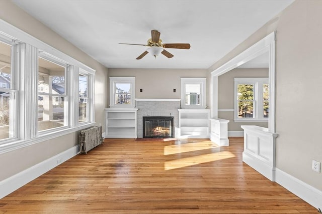 unfurnished living room with plenty of natural light, radiator, light hardwood / wood-style floors, and a brick fireplace