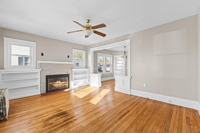 unfurnished living room featuring ceiling fan with notable chandelier, a fireplace, and light hardwood / wood-style flooring