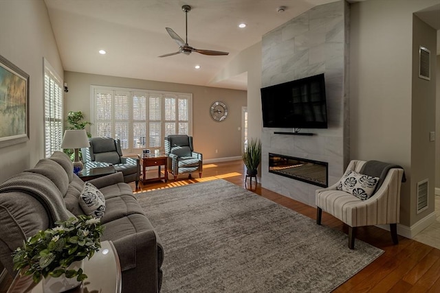 living area with lofted ceiling, visible vents, a tiled fireplace, wood finished floors, and plenty of natural light