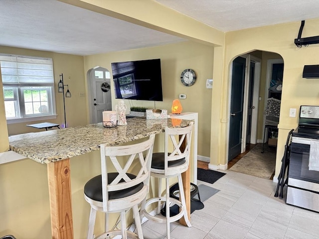 169 Beauchamp Ter, Chicopee, MA 01020 - kitchen with arched walkways, stainless steel electric range, a breakfast bar, and light stone counters