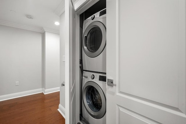 laundry area featuring stacked washer / dryer, dark wood-type flooring, crown molding, baseboards, and laundry area