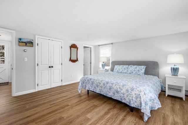 bedroom with a baseboard heating unit, a closet, baseboards, and wood finished floors