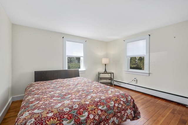 bedroom with a baseboard heating unit, multiple windows, and hardwood / wood-style flooring