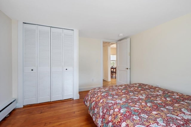 bedroom with baseboard heating, light wood-type flooring, and a closet
