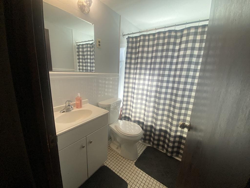 bathroom featuring tile patterned flooring, toilet, a shower with shower curtain, wainscoting, and vanity