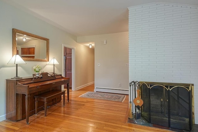 living room with a baseboard heating unit, light wood-type flooring, a brick fireplace, and baseboards
