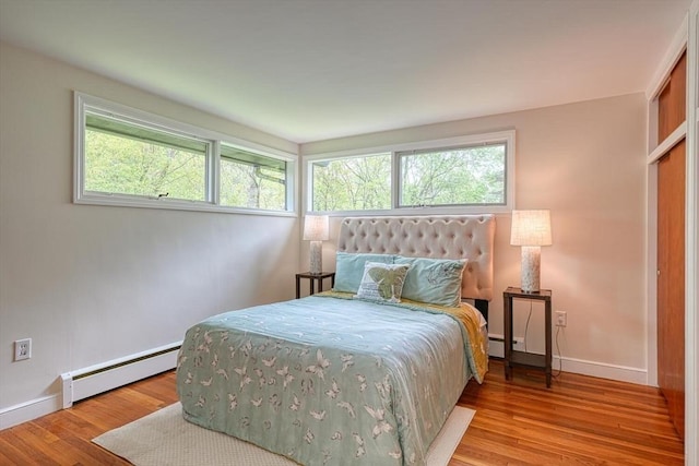 bedroom featuring a baseboard radiator, baseboards, multiple windows, and wood finished floors