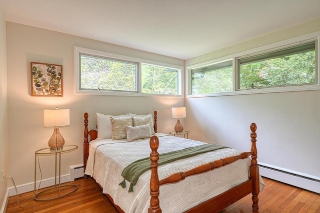 bedroom featuring a baseboard radiator, multiple windows, and wood finished floors