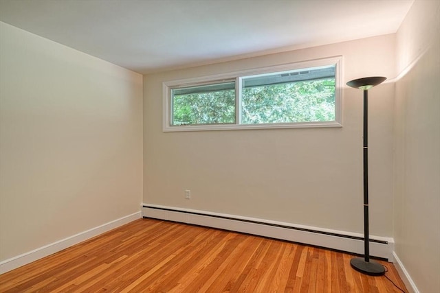 unfurnished room with baseboard heating, light wood-style flooring, and baseboards