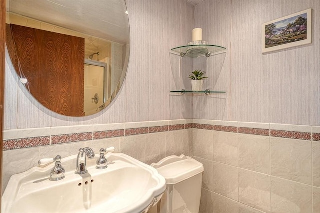 bathroom with a sink, wallpapered walls, a wainscoted wall, toilet, and tile walls
