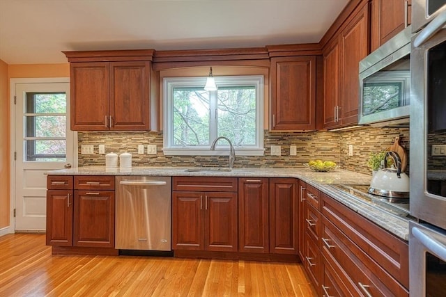 kitchen featuring stainless steel appliances, a sink, light wood-style flooring, and light stone countertops