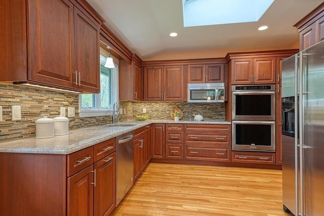 kitchen featuring appliances with stainless steel finishes, light wood-style floors, a skylight, lofted ceiling, and light stone countertops