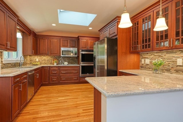 kitchen with a sink, appliances with stainless steel finishes, a skylight, light wood-style floors, and a peninsula