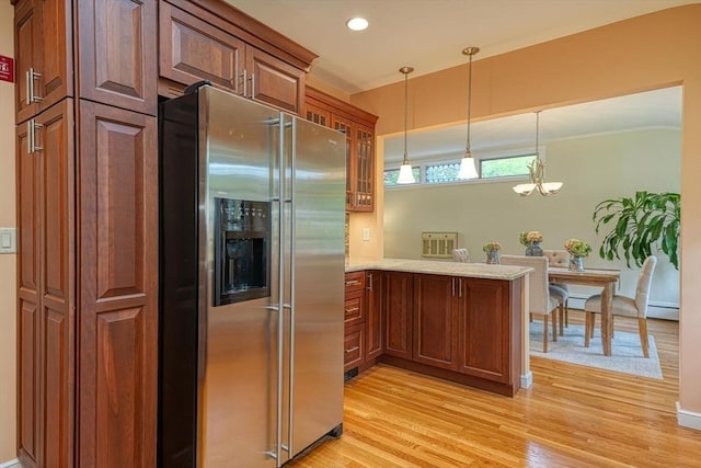 kitchen featuring stainless steel fridge, light wood finished floors, glass insert cabinets, a peninsula, and pendant lighting