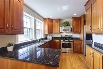 kitchen featuring light wood-type flooring, kitchen peninsula, appliances with stainless steel finishes, and dark stone counters