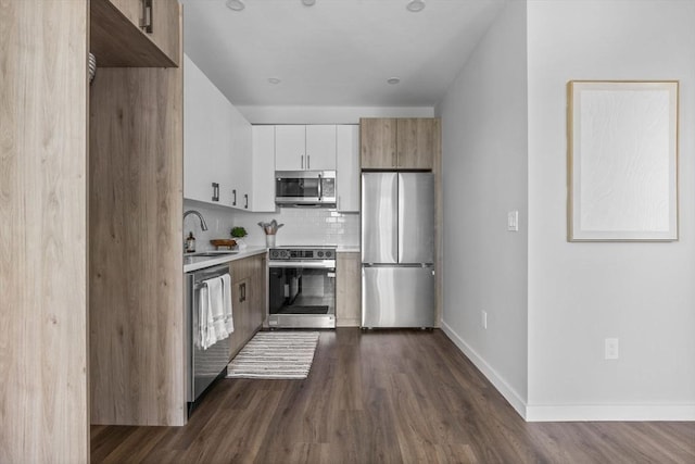 kitchen featuring appliances with stainless steel finishes, a sink, light countertops, tasteful backsplash, and dark wood-type flooring