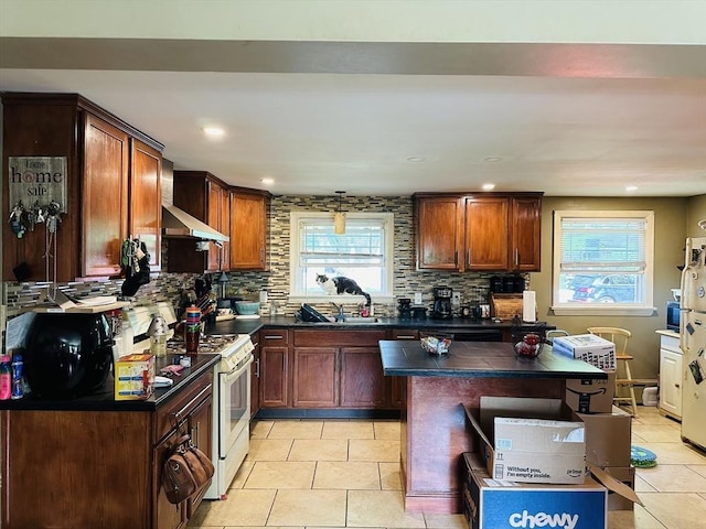 kitchen with white range with gas stovetop, dark countertops, decorative backsplash, light tile patterned floors, and wall chimney exhaust hood