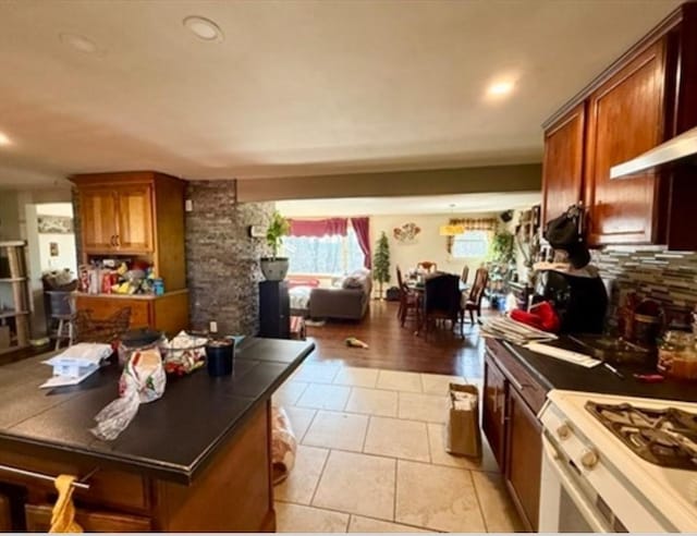 kitchen with gas range, tasteful backsplash, brown cabinetry, dark countertops, and light tile patterned floors