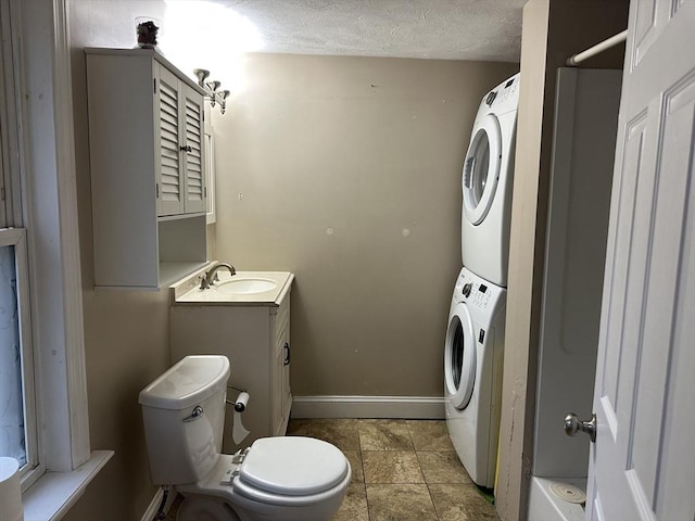 bathroom featuring a textured ceiling, stacked washer / dryer, baseboards, toilet, and vanity