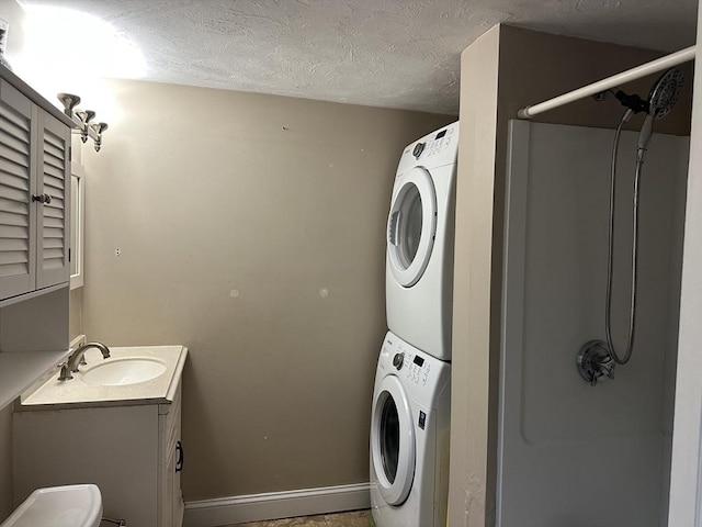 laundry area with a sink, a textured ceiling, stacked washer / dryer, laundry area, and baseboards