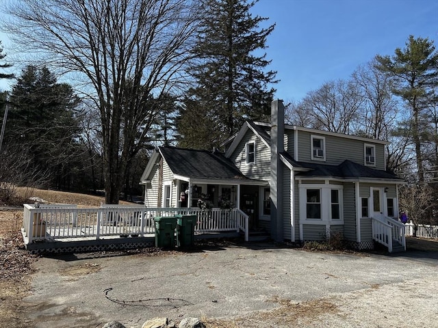 view of front of home with a wooden deck, a shingled roof, and a chimney