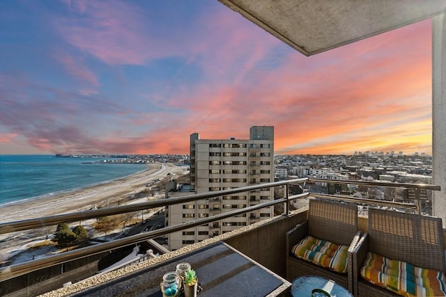 balcony at dusk featuring a water view and a view of the beach