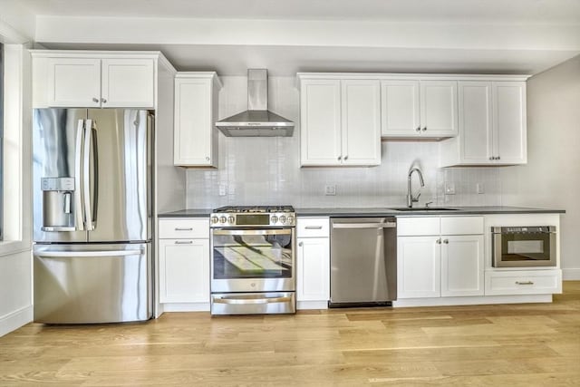 kitchen with sink, white cabinets, stainless steel appliances, and wall chimney range hood