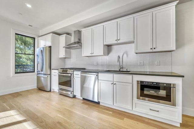 kitchen with wall chimney exhaust hood, white cabinetry, sink, and appliances with stainless steel finishes