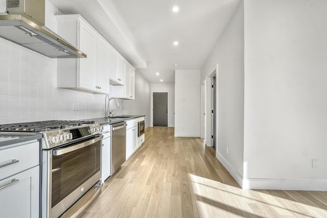 kitchen featuring wall chimney range hood, sink, light hardwood / wood-style flooring, white cabinetry, and stainless steel appliances