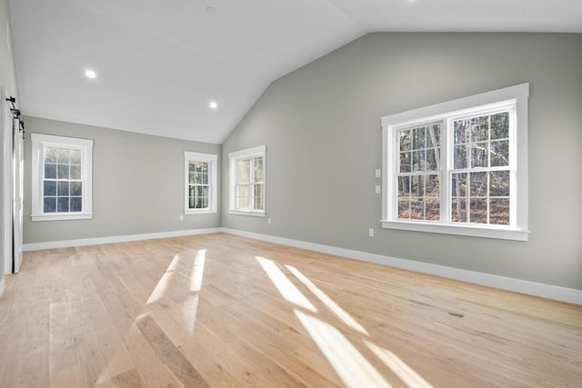 unfurnished room with a barn door, light hardwood / wood-style flooring, and vaulted ceiling