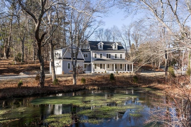 rear view of property with a porch, a garage, and a water view