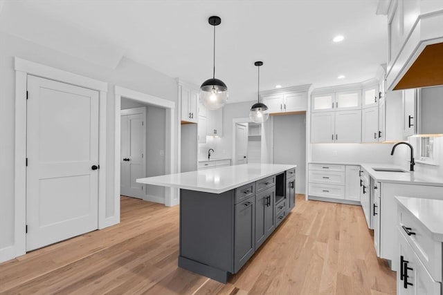 kitchen with gray cabinetry, a center island, white cabinets, sink, and light wood-type flooring