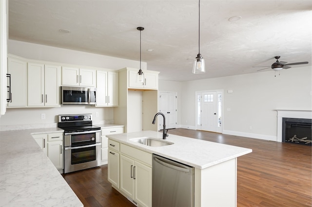 kitchen with hanging light fixtures, sink, a kitchen island with sink, dark wood-type flooring, and appliances with stainless steel finishes