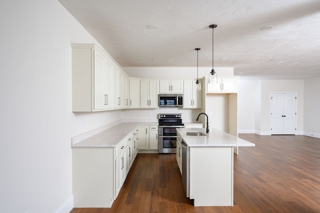 kitchen with stainless steel appliances, dark wood-type flooring, sink, hanging light fixtures, and a center island with sink