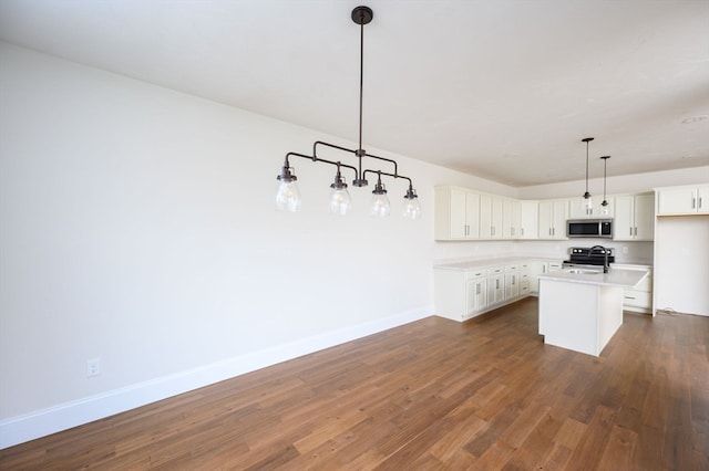 kitchen featuring dark wood-type flooring, a center island with sink, decorative light fixtures, white cabinets, and appliances with stainless steel finishes